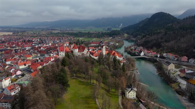 Breathtaking aerial view of Fuessen, Germany, showcasing St. Mang Church, the majestic Hohes Schloss, and the Lech River. The charming medieval town is surrounded by lush greenery and Bavarian Alps. 
