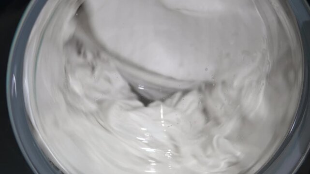 White laundry washing machine cycle spinning. Close-up top view of white clothes spinning inside a washing machine drum during a wash cycle, showcasing the rotating motion of the laundry with water