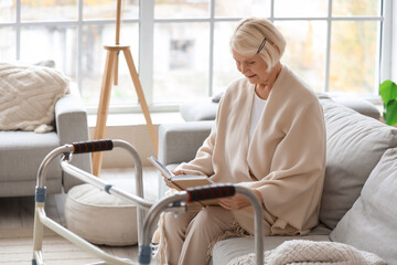 Senior woman with walker reading book on sofa at home