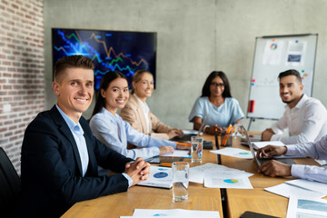 Colleagues of various backgrounds gather around a desk in a bright office.