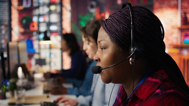 Employee talking with customer using headphones microphone to identify new sales opportunities. Account manager in office using audio headset, bonding with client to generate leads, camera B close up - Powered by Adobe