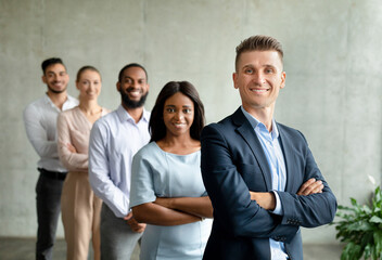 Successful businessman and businesswoman stand confidently in front of a grey wall, joined by their multiethnic colleagues. They smile while showing teamwork and unity in the office environment.