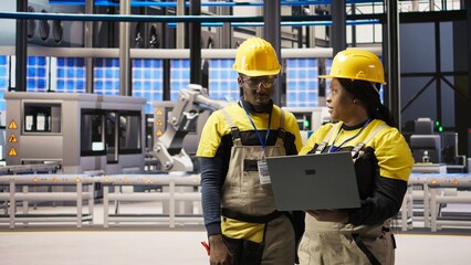 Smart factory engineering team using laptop to calibrate high tech machinery and analyze sensor...