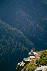 Young woman blogger taking selfie on cliff edge with breathtaking forest view in Fagaras Mountains, Romania. Transfagarasan Highway. Freedom, solo travel concept