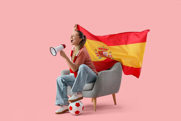 Female soccer fan with Spanish flag shouting into megaphone in armchair on pink background
