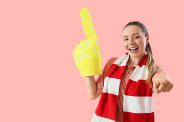 Female soccer fan with foam hand pointing at viewer on pink background