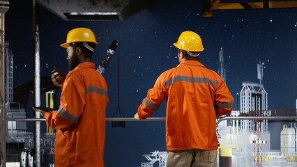 Worker in hard hat conducts system inspections on offshore drilling rig from industrial platform,...