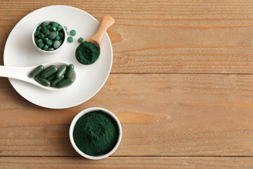 Bowls of spirulina powder with tablets and capsules on wooden background