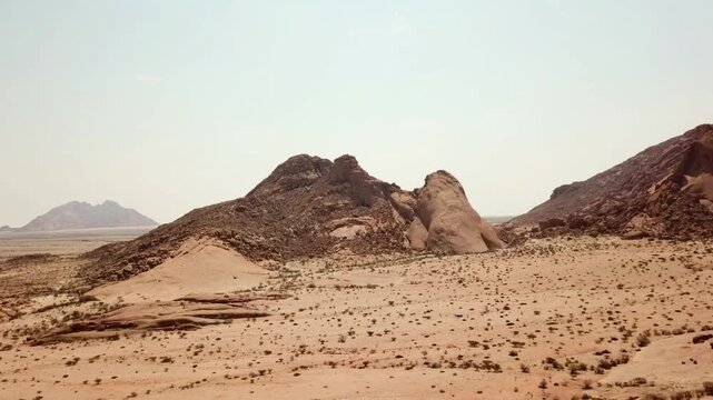 Cinematic aerial drone pan revealing the full granite mountain range of Spitzkoppe in the Namib Desert, Namibia. Smooth panoramic motion showcasing dramatic rock formations, rugged desert terrain, and