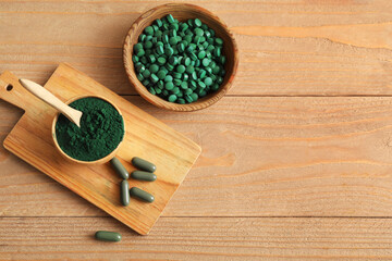 Bowls of spirulina powder and tablets with capsules on wooden background