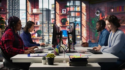 Call center worker speaking in audio headset microphone, using remote access tools. Woman in customer center assisting clients with installing software, communicating through headphones mic, camera B