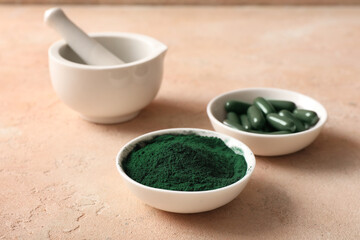 Bowls of spirulina powder and capsules with mortar on beige grunge background