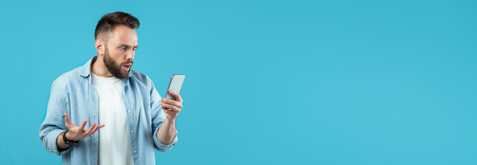 A man with a beard displays shock and confusion as he looks at his smartphone. He is wearing a...