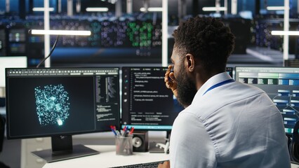 Server farm computer scientist interprets AI generated data analytics graphs. African american man in data center using artificial intelligence program showing predictive system metrics, camera A