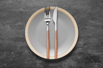 Plate with silver fork and knife on black grunge background