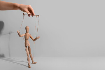 Hand of puppeteer manipulating marionette on light background