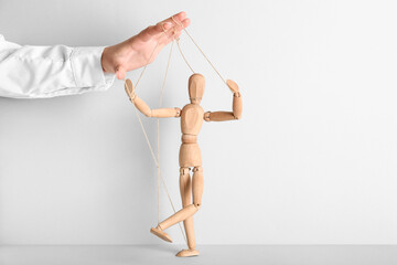 Hand of puppeteer manipulating marionette on light background