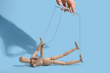 Hand of puppeteer manipulating marionette on blue background