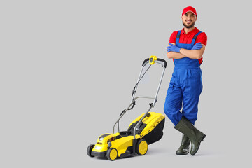 Male gardener with lawn mower on light background