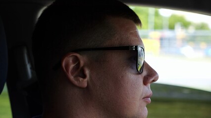 Profile of confident man driving a motor car at town. Male face of male driver in sunglasses looking concentrated to urban road while riding automobile. Slow motion