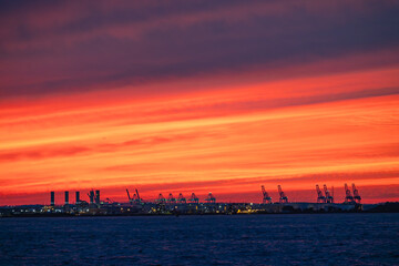 Dramatic red sunset over industrial port with container cranes on the coastline