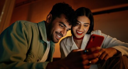 Couple using smartphone together while smiling in warm indoor evening light