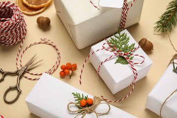 Gift boxes wrapped in eco paper with Christmas decorations, rowan berries, dried oranges and packing materials on beige background © Pixel-Shot