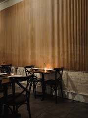 Intimate restaurant corner with wooden slat wall, candlelit table settings, and modern black chairs in a warm, minimalist dining space