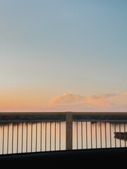 Obraz premium Sunset sky and calm river viewed through car window with bridge railing in foreground
