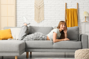 Beautiful young woman using laptop on grey sofa at home