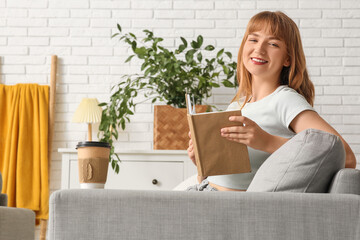 Beautiful young woman reading book on grey sofa at home