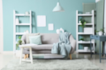 Blurred view of living room with grey sofa, table and shelving units near mint wall