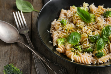Bowl of delicious fusilli pasta with broccoli and basil leaves on wooden background, closeup