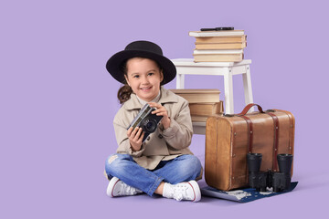 Fototapeta premium Cute little detective with photo camera and adventure books sitting on lilac background
