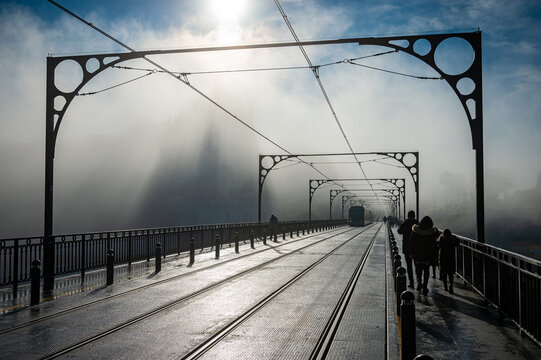 Tram on Luis I bridge emerging from the fog shrouding a church tower in Porto, Portugal