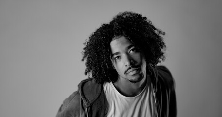 Obraz premium Studio portrait of a young man with curly hair in black and white. This fashion and beauty shot on a gray background features a headshot of a male model looking up at the camera with a serious express