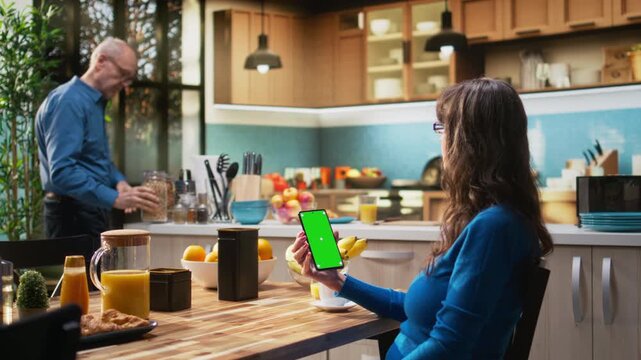 Mockup display on phone at kitchen table with elderly woman smiling and relaxing, serving coffee and meal for breakfast at the table. Fun retirement lifestyle from comfortable rustic home. Camera A.