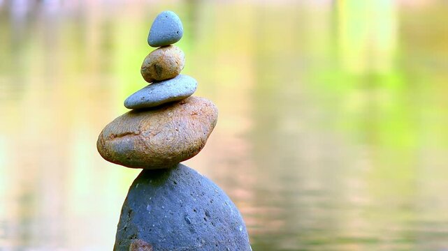 Tower of rocks balancing on top of each other with quiet water reflecting thickets of plants on background. Stones stacked into pyramid on bank of tropical pond. Video with sound of birds singing.