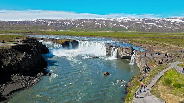 Drone footage of Godafoss Waterfall surrounded by rocky cliffs in North Iceland. The strong current flows over the wide horseshoe-shaped falls.