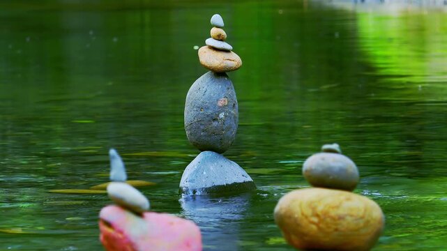 Close-up shot of rocks stacked on top of each other and placed in quiet jungle lake. Meditation scene with stone piles by side of water, balance symbol, harmony and tranquility. Sound of birds singing