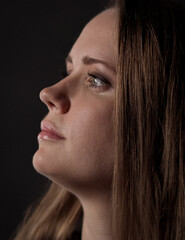Fototapeta premium Studio profile portrait of a young woman with long brown hair on a dark background. This image is suitable for fashion beauty and advertising projects.