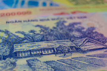 This image shows a close-up of Vietnamese Dong banknotes. Specifically, it highlights the blue-toned 200,000 VND note, featuring a traditional landscape with a rural house and lush vegetation.