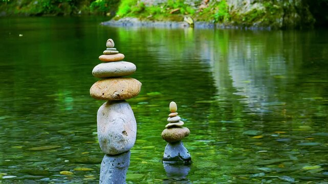 Tower of rocks balancing on top of each other with quiet water reflecting thickets of plants on background. Stones stacked into pyramid on bank of tropical pond. Harmony and tranquility symbol
