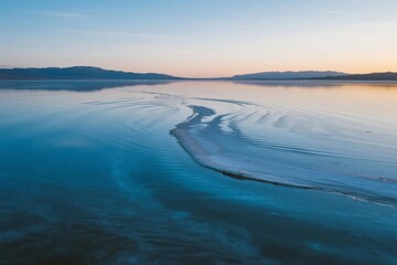 Aerial view of a calm lake with ice formations at sunrise, reflecting the sky and distant hills