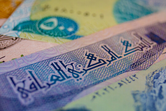 A macro shot of an Iraqi Dinar note featuring blue and green hues, prominent Kufic Arabic calligraphy for "Central Bank of Iraq," intricate geometric patterns, and fine microprinting for security.