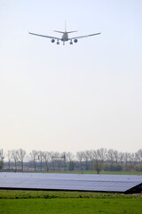 A plane descending and flying low over a field with solar panels, Amsterdam, The Netherlands