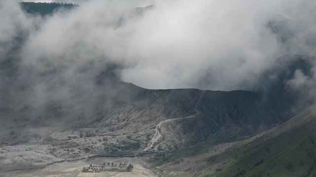 Amazing landscape with Pura Luhur Poten hindu temple near Mount Bromo. Clouds of thick white smoke emitted by erupting volcano Tengger Semeru National Park. East Java, Indonesia. Camera zooming out