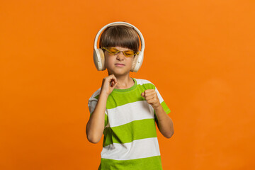 Happy smiling preteen child boy in headphones listening music dancing disco fooling around having fun expressive gesticulating hands relaxing on party making funny moves. Kid on orange background