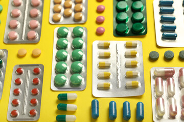 Different pills in blister packs on yellow background, closeup