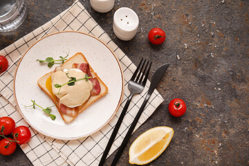 Plate of delicious egg Benedict with bacon and cherry tomatoes on dark background